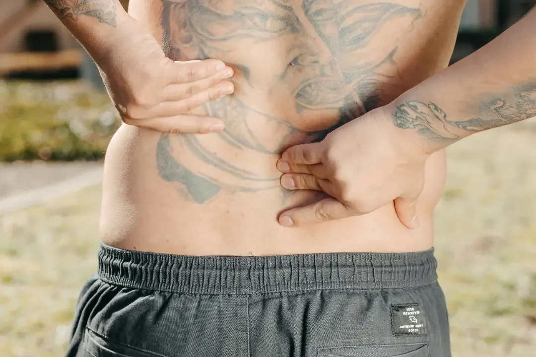 Tatuoitu mies kärsii alaselän kivusta ja etsii ammattitaitoista apua vaivaansa.